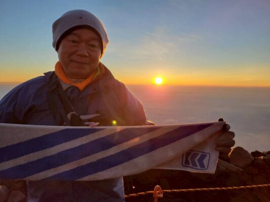 ご来光をバックに当社マフラータオルをを手にする社長の記念写真